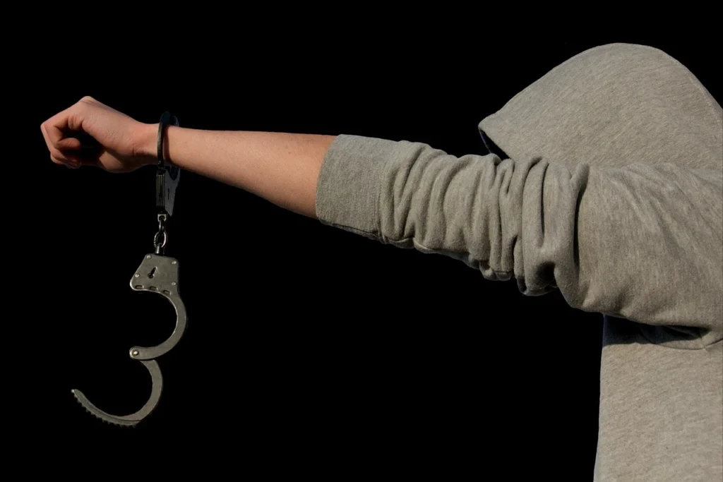 A minor holding their hand out with a handcuff dangling.